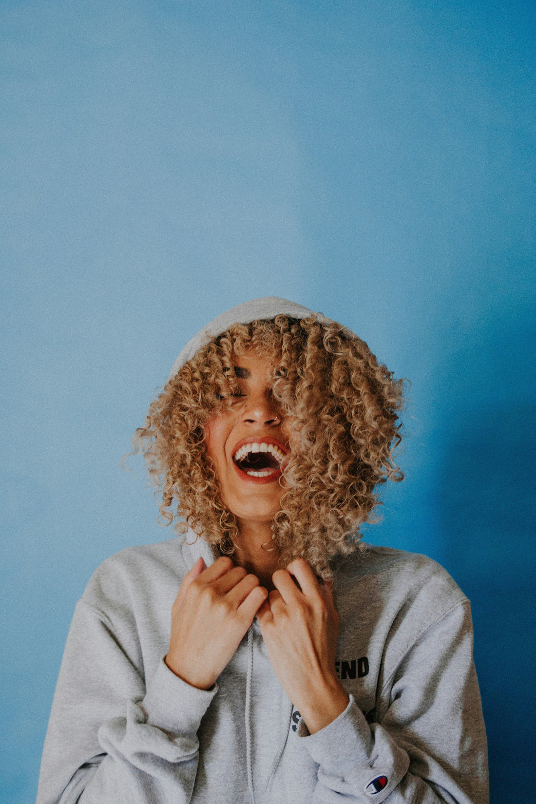 A woman with curly hair laughing with the blue background