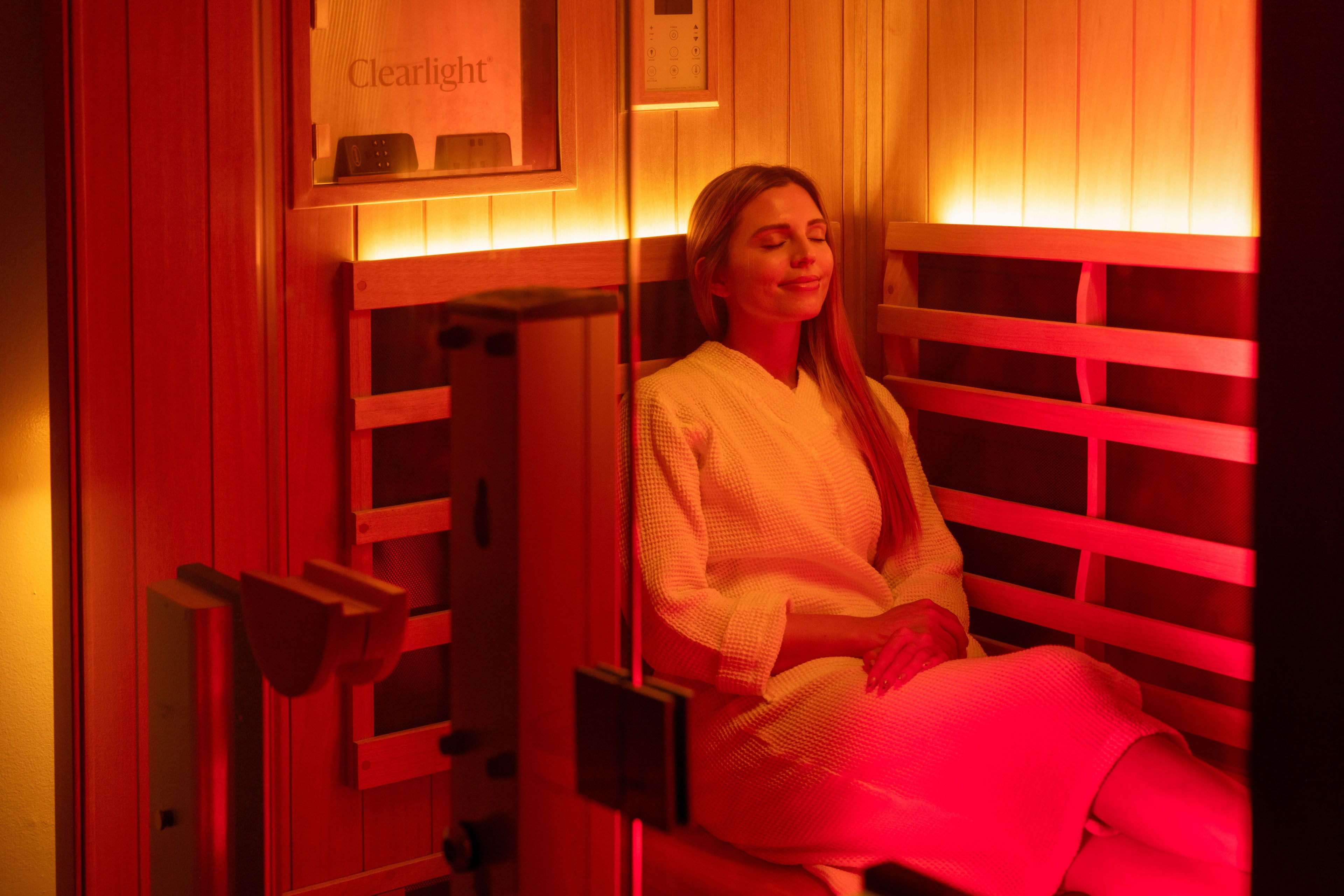 A woman sitting in a Clearlight infrared sauna with warm rd lighting
