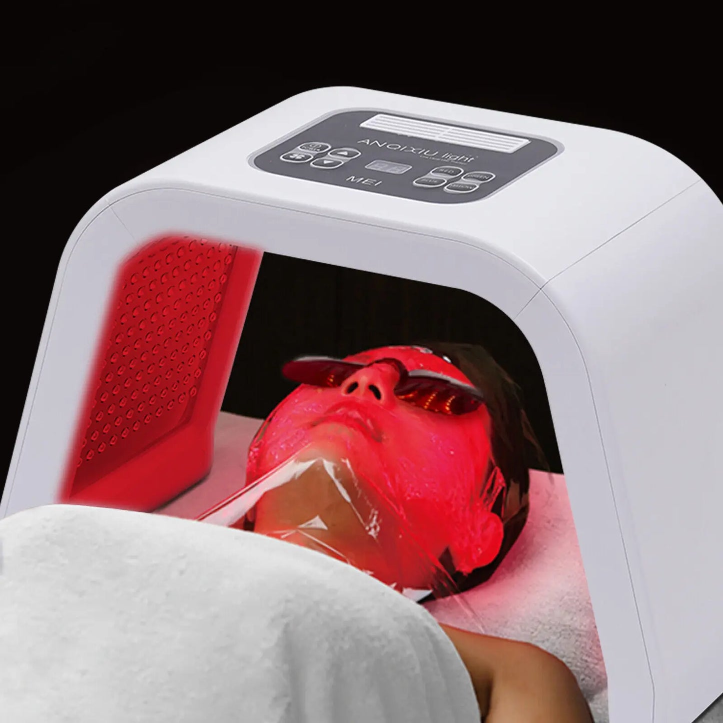 Person receiving red light therapy under a white device with digital display.